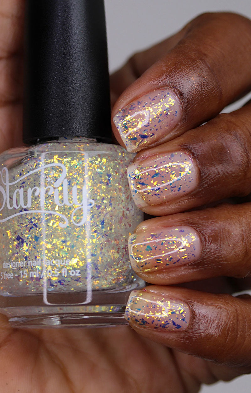Person holding a bottle of Starrily nail polish with gold flakie effect nails.