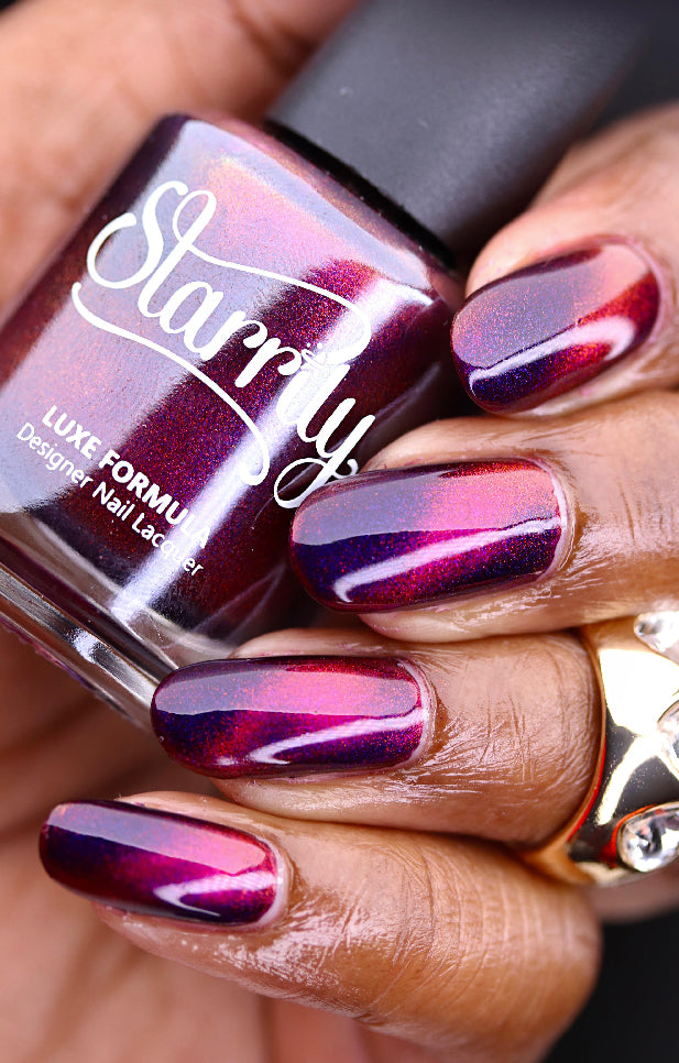 A close-up image of a hand with nails painted in a purple and copper magnetic effect color, holding a nail polish bottle with the brand name 'Starrily' on it.